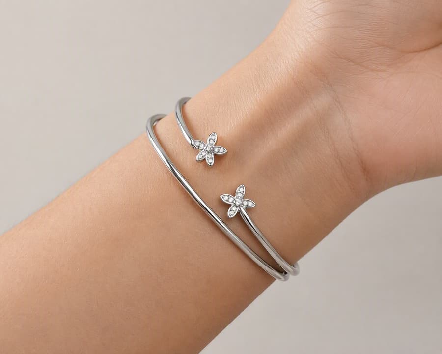 Two slim silver-tone cuffs with flower ends resting against the inside of a wrist